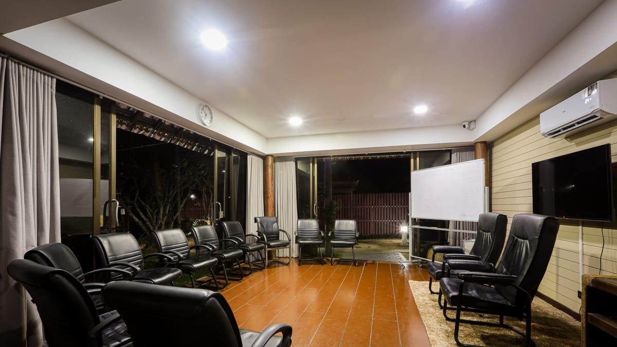 Empty room with black chairs around a wood floor, a whiteboard and glass doors to the garden at Jintara Rehab