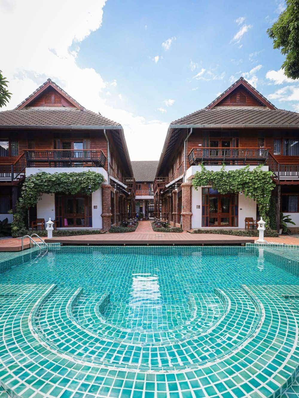 Teal-tiled pool framed by two-storey Lanna timber buildings