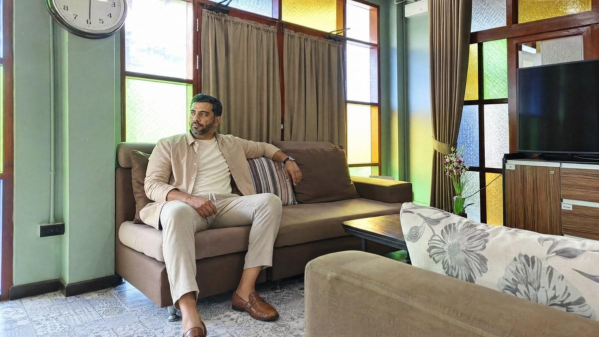 A man sits alone on a sofa by the stained-glass windows at Jintara Rehab in Chiang Mai, unhurried, during a residential stay