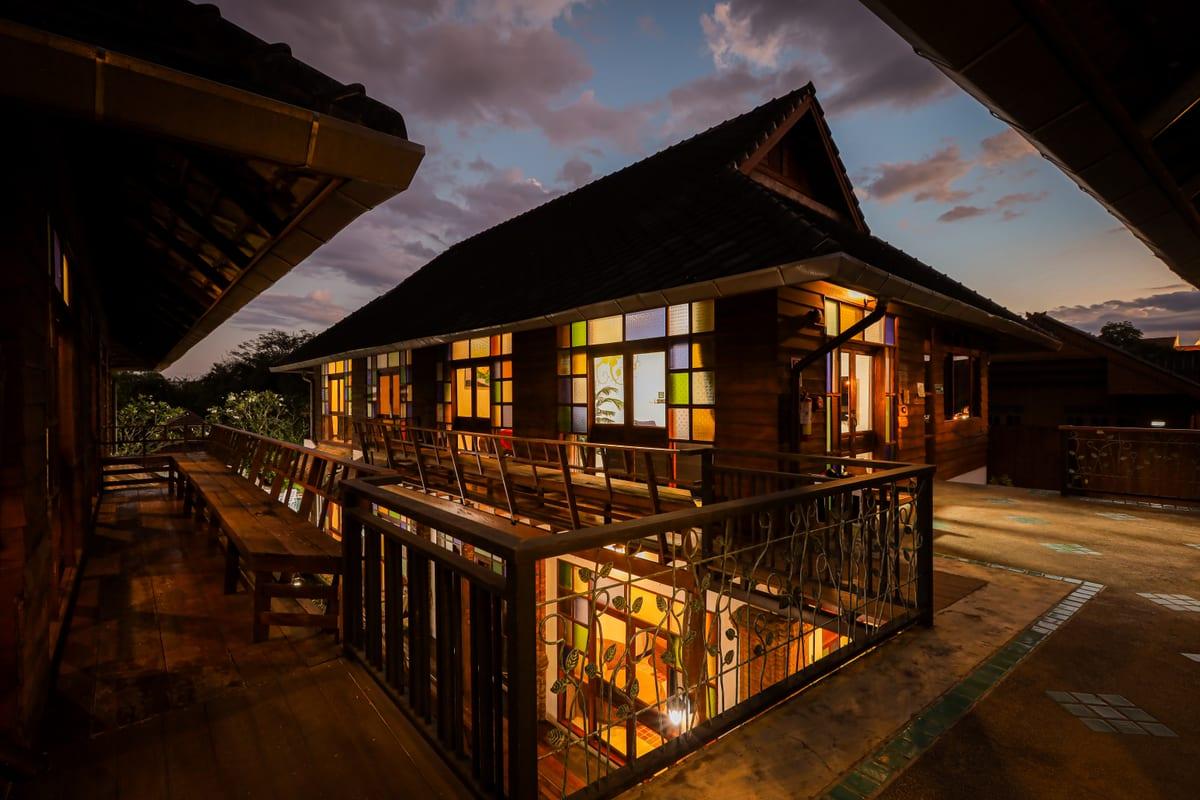 Lanna-style building at Jintara Rehab at dusk with glowing stained glass windows against evening sky