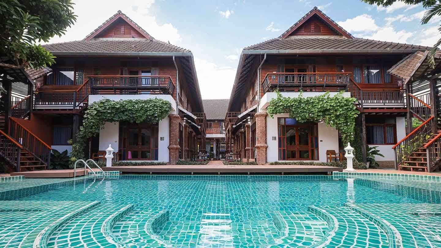 Two Lanna-style buildings with teak balconies flanking a turquoise pool at Jintara Rehab Chiang Mai