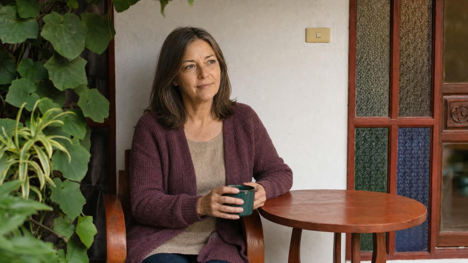 A woman with a cup of tea on a vine-covered garden porch at Jintara Rehab Chiang Mai during a supervised taper