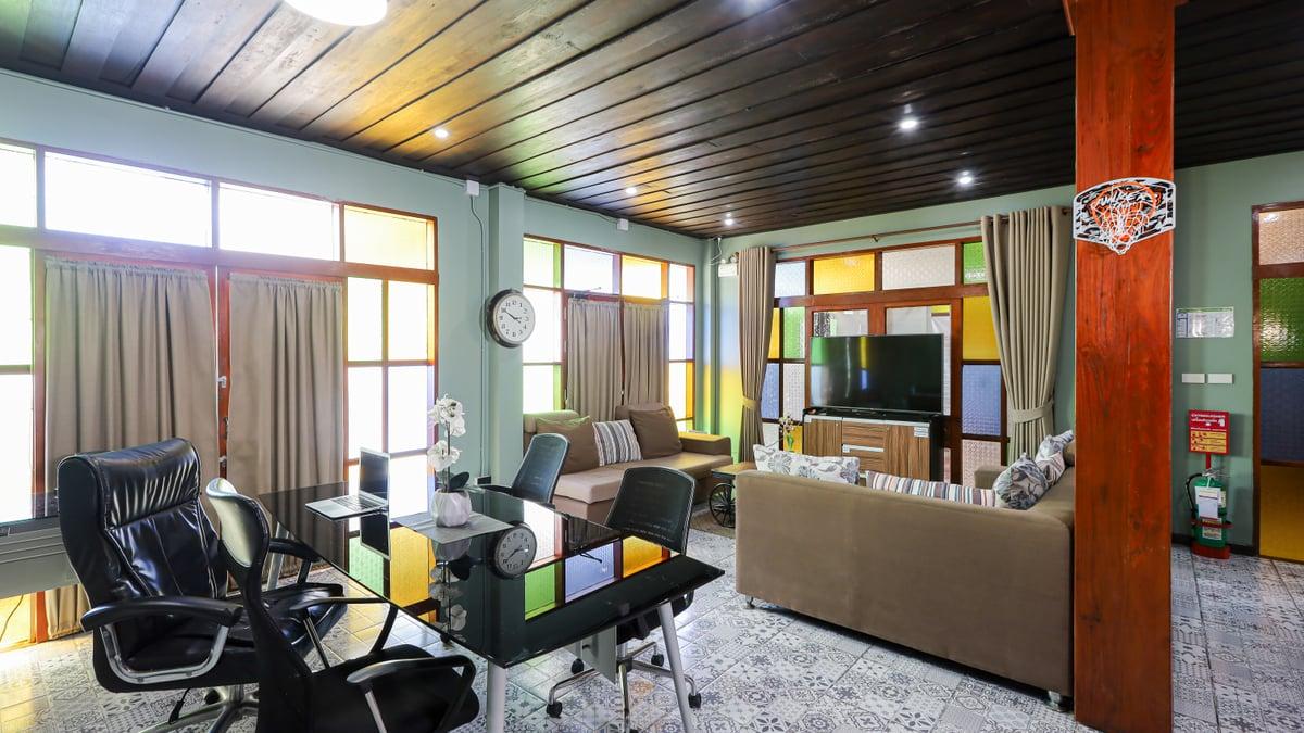 An empty lounge with sofas, a glass desk and coloured glass windows at Jintara Rehab