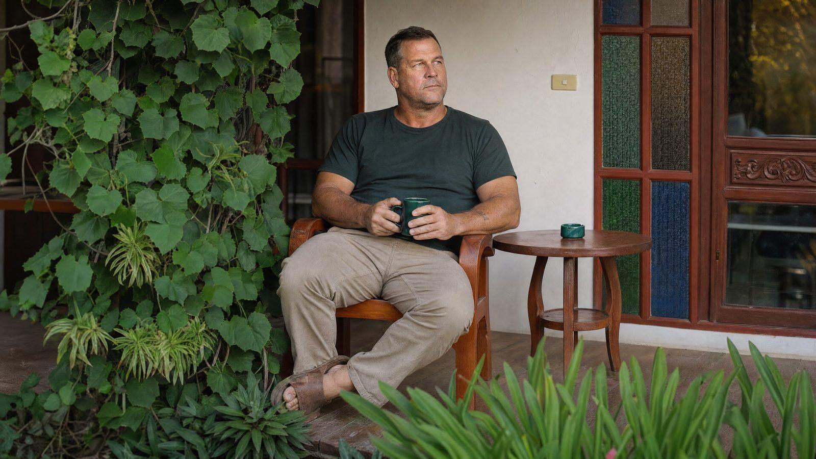 A man sits with a coffee on the veranda at Jintara Rehab in Chiang Mai, Thailand, in the residential program his family arranged