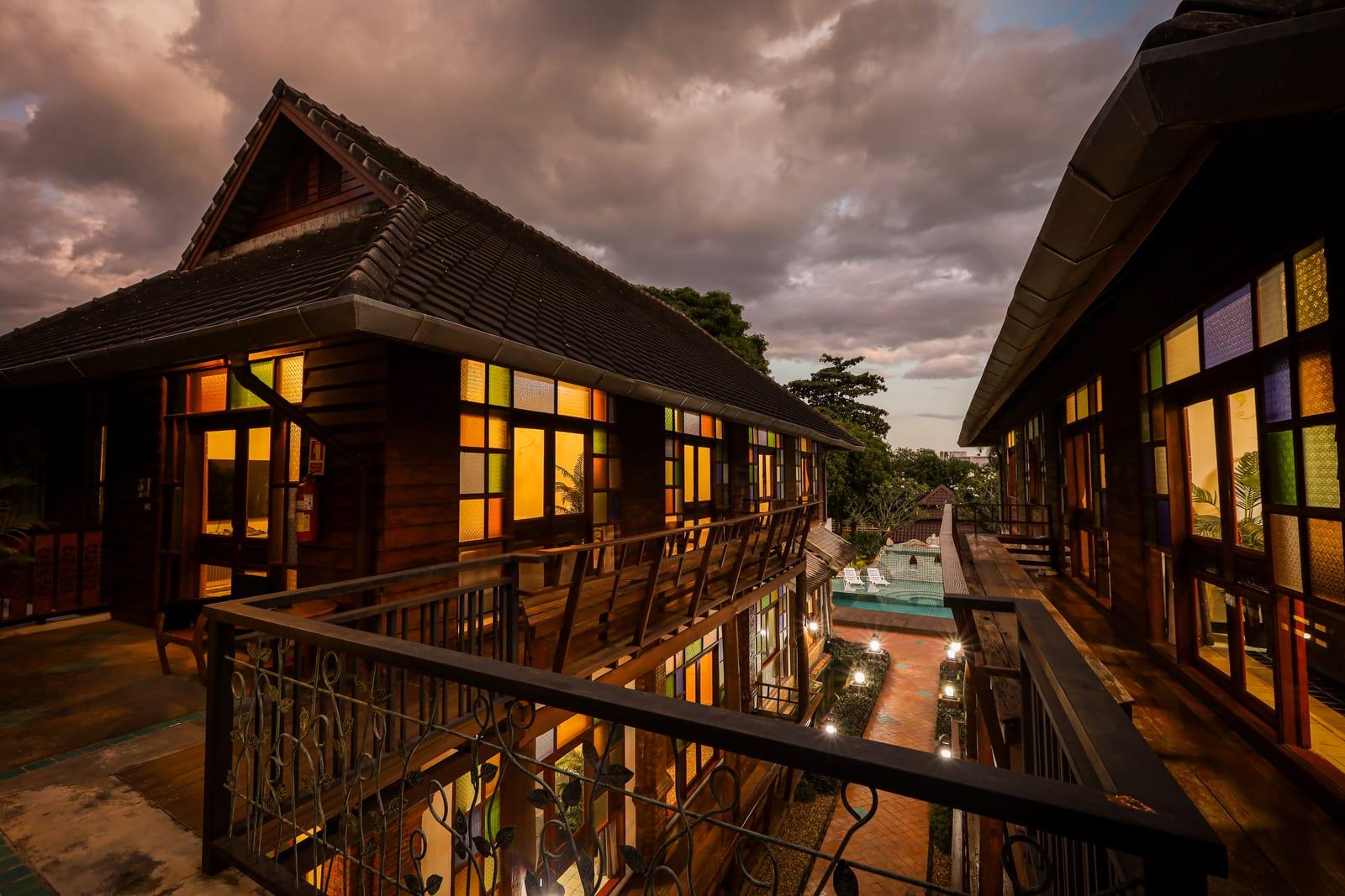 Pool and teak buildings at dusk at Jintara Rehab in Chiang Mai, amber stained glass lit