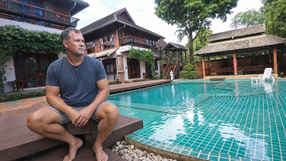 Man sitting on the timber pool deck beside the teal mosaic pool at Jintara Rehab Chiang Mai