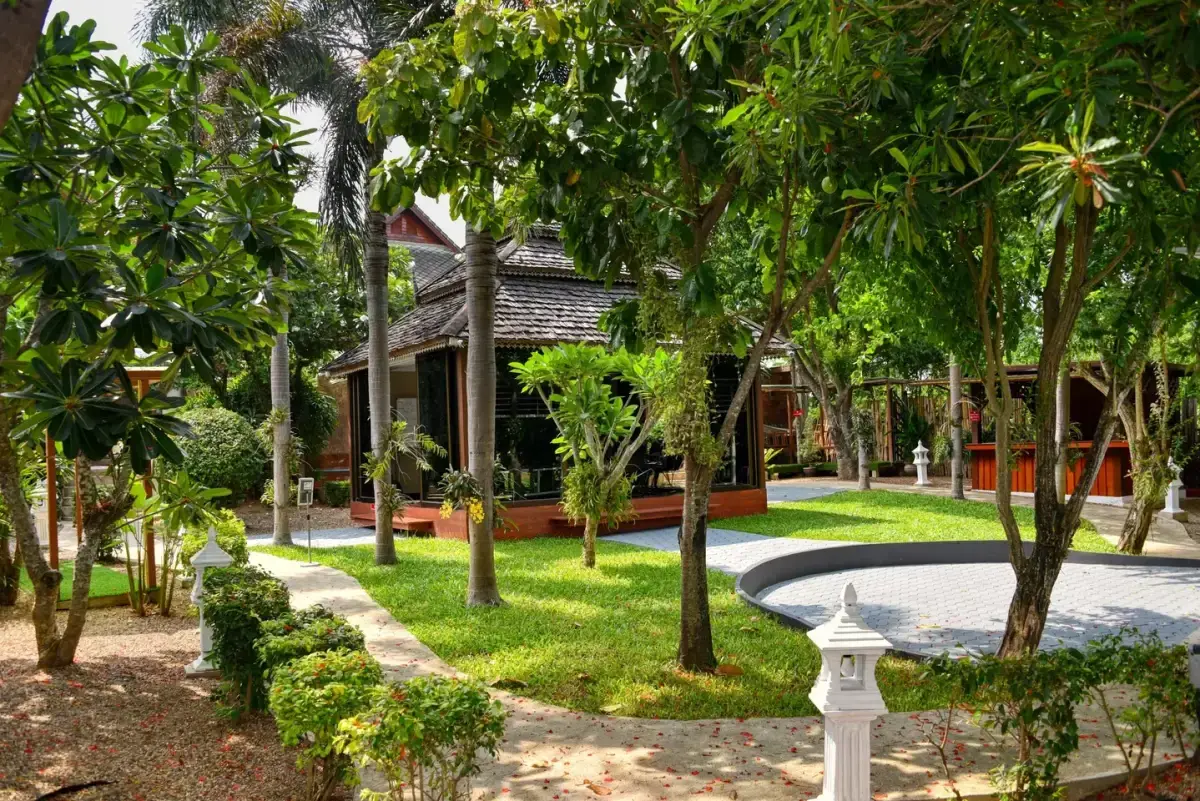 Lush tropical garden at Jintara Rehab in Chiang Mai, with Lanna-style buildings visible