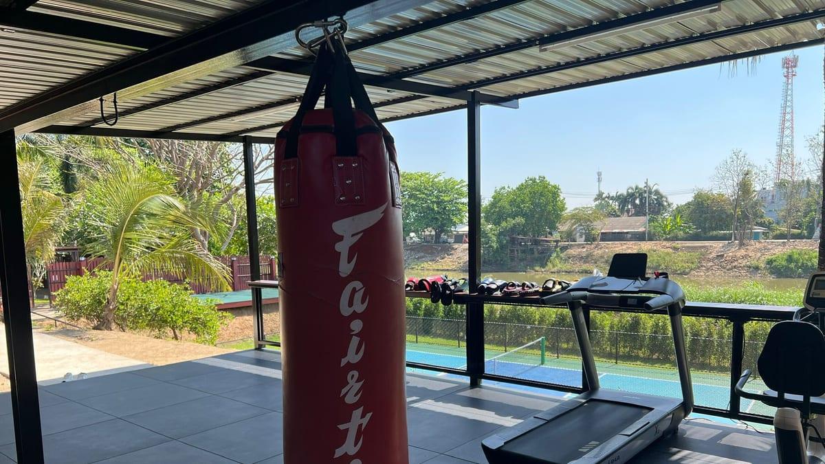 Jintara's red boxing bag hanging from the covered gym frame beside the treadmill