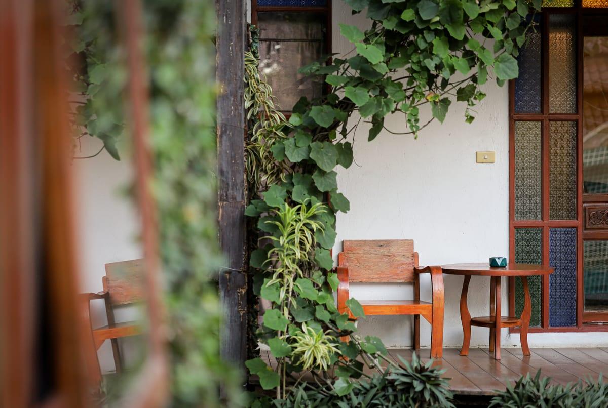 Private outdoor seating area with wooden chairs through tropical vines at Jintara Rehab Chiang Mai