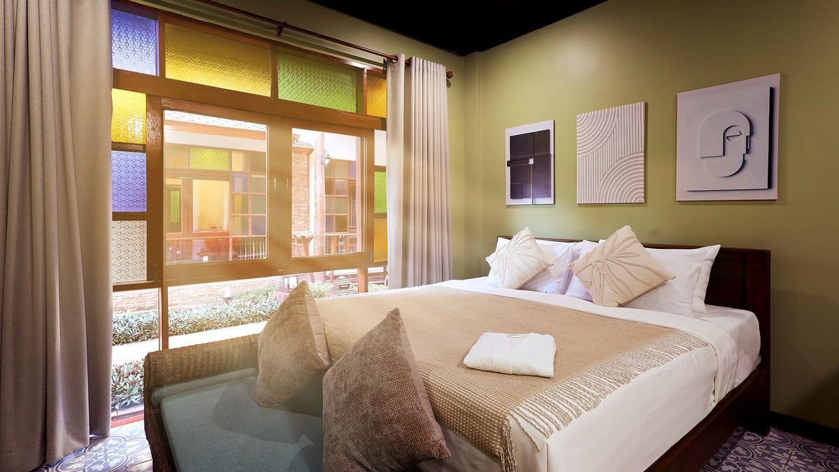 Private bedroom with a made bed, stained glass windows and a garden view