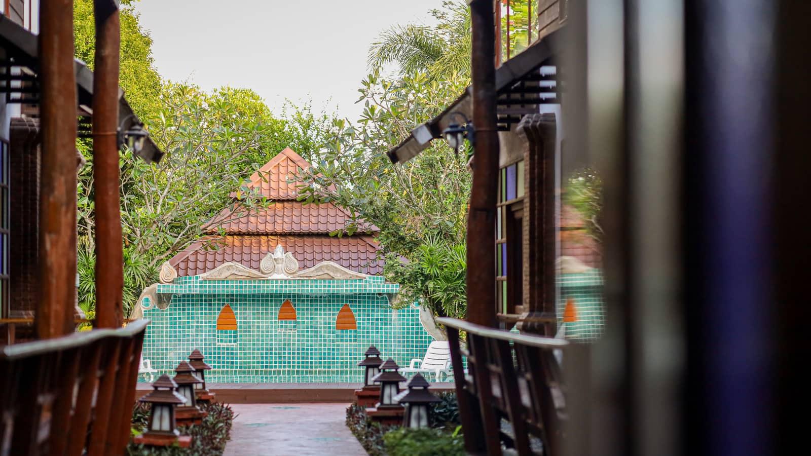 Covered teak walkway leading to teal pool at Jintara Rehab Chiang Mai with lanterns