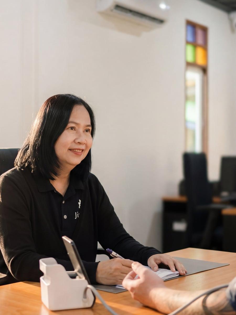 Jintara clinical nurse conducting intake consultation at desk with blood pressure monitor Chiang Mai