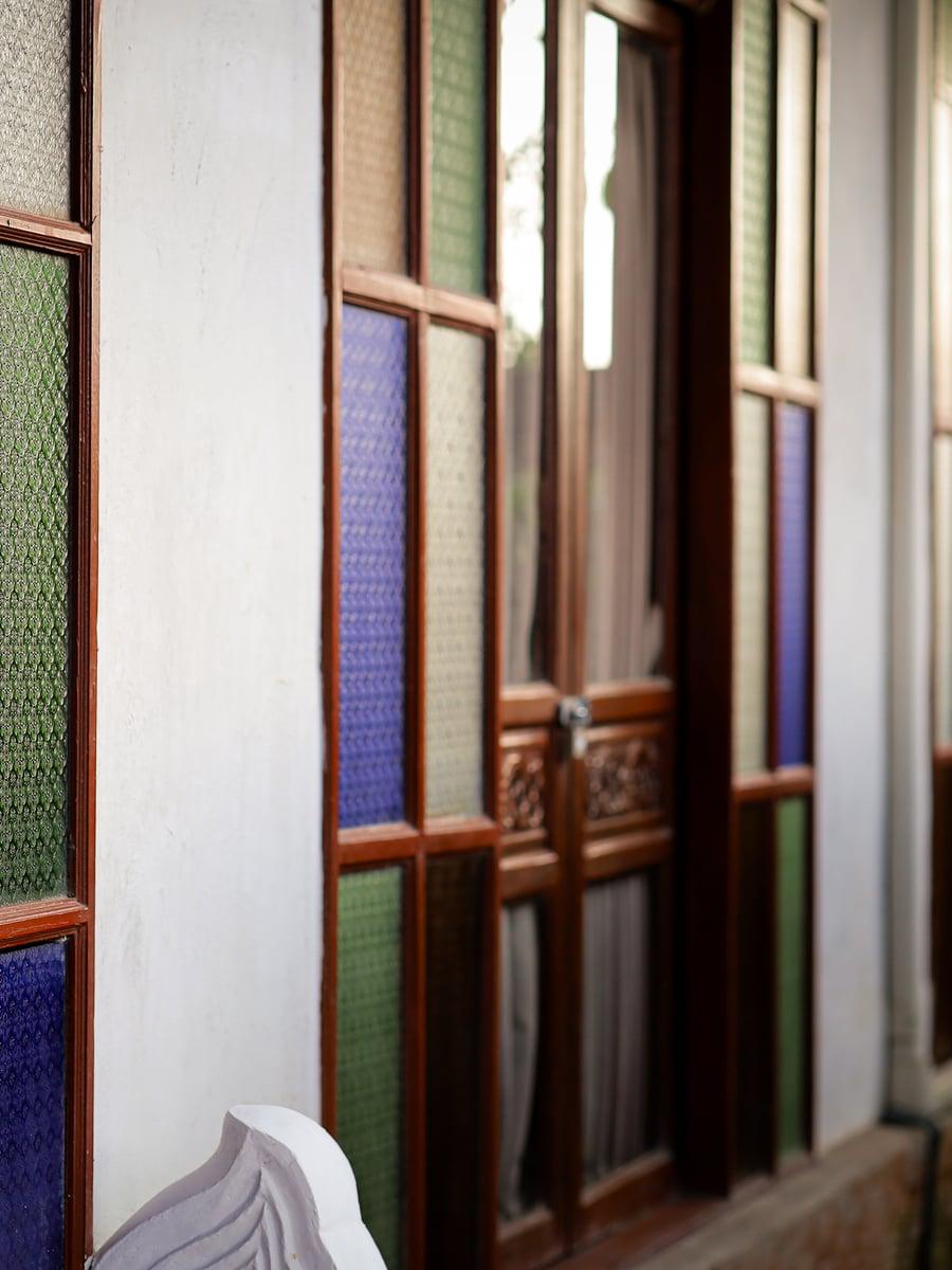 Traditional Lanna carved wooden door with coloured stained glass panels at Jintara Rehab Chiang Mai trauma therapy