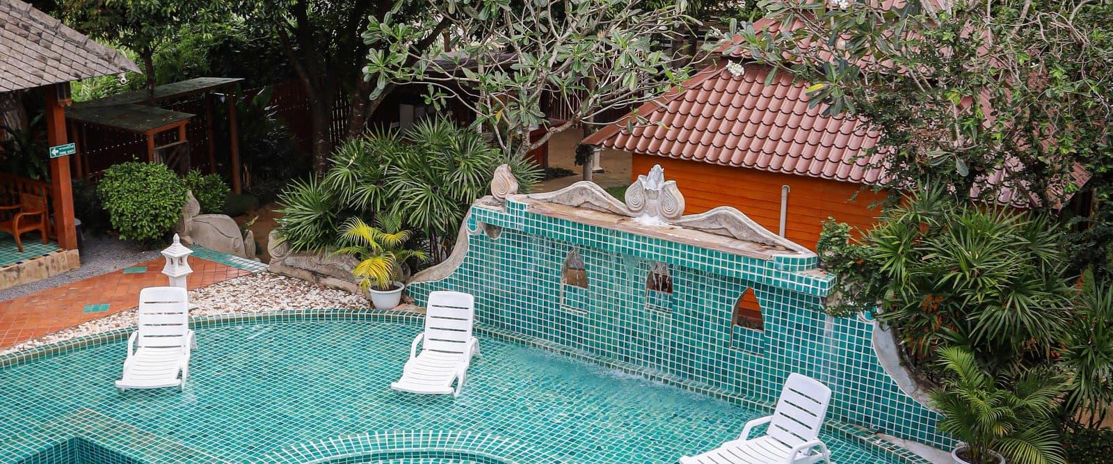 A teal mosaic pool surrounded by tended gardens and Lanna buildings in Chiang Mai