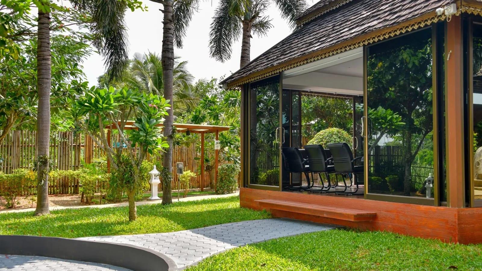 Glass-walled garden pavilion and tropical lawn at Jintara Rehab Chiang Mai in daylight