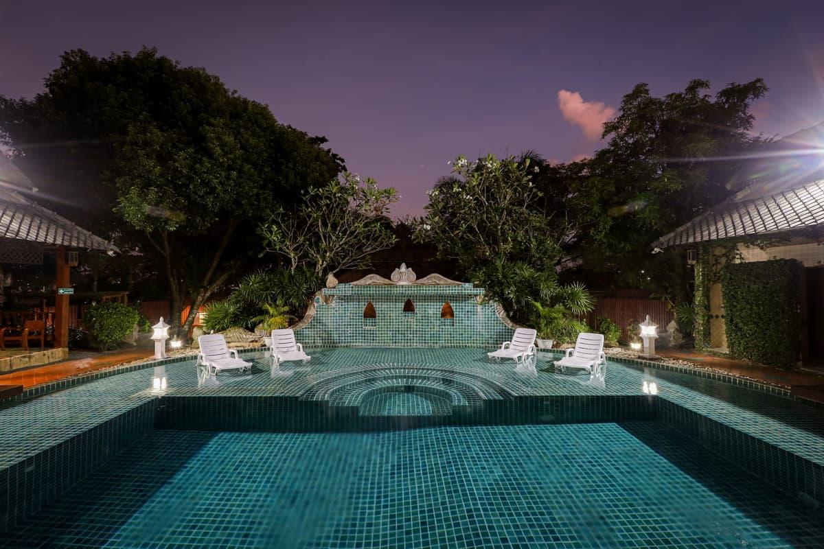 Twilight shot of the teal mosaic pool at Jintara Rehab Chiang Mai with white sun loungers
