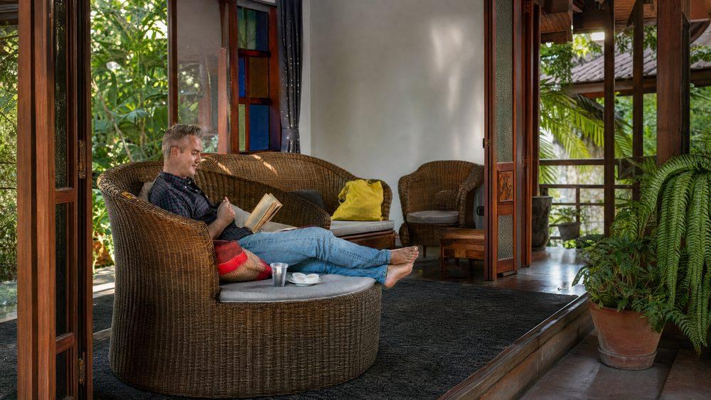 Male client resting and reading on wicker veranda sofa at Jintara Rehab Chiang Mai during opioid withdrawal recovery