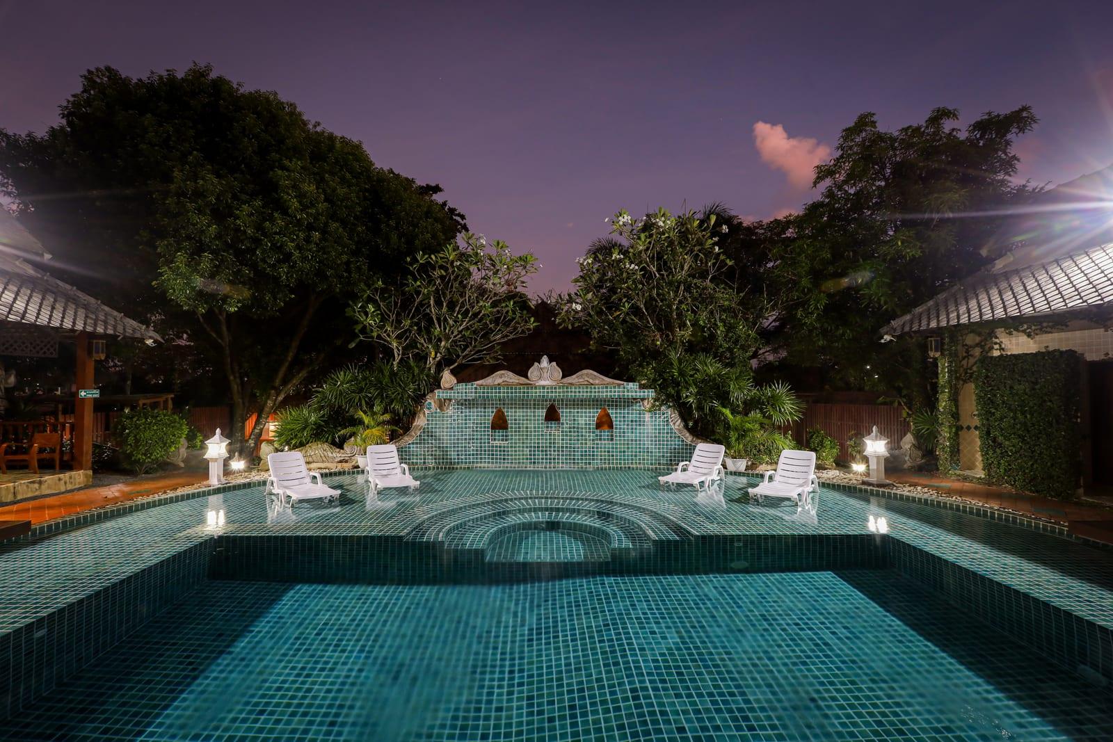 Teal pool with symmetrical teak buildings and stained glass windows at twilight at Jintara Rehab Chiang Mai