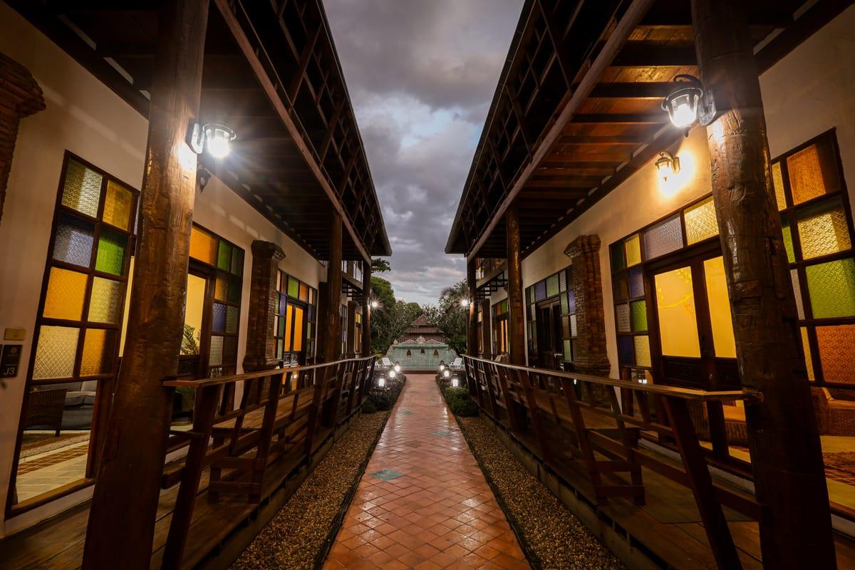 Evening walkway between Lanna teak buildings with stained glass and lanterns at Jintara Rehab Chiang Mai Thailand
