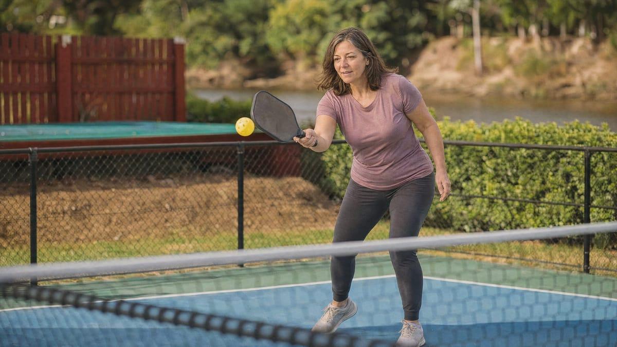 Woman mid-rally on the riverside pickleball court at a Chiang Mai rehab in daylight