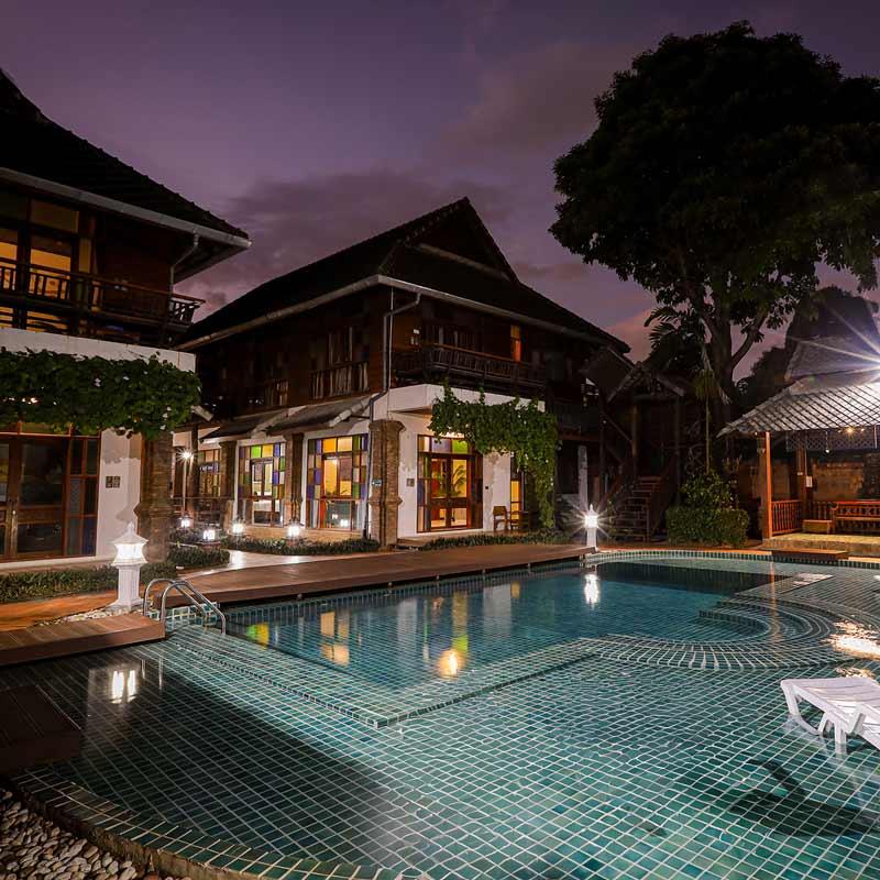 Jintara Rehab Lanna building and pool at dusk with stained glass and vine-covered walls