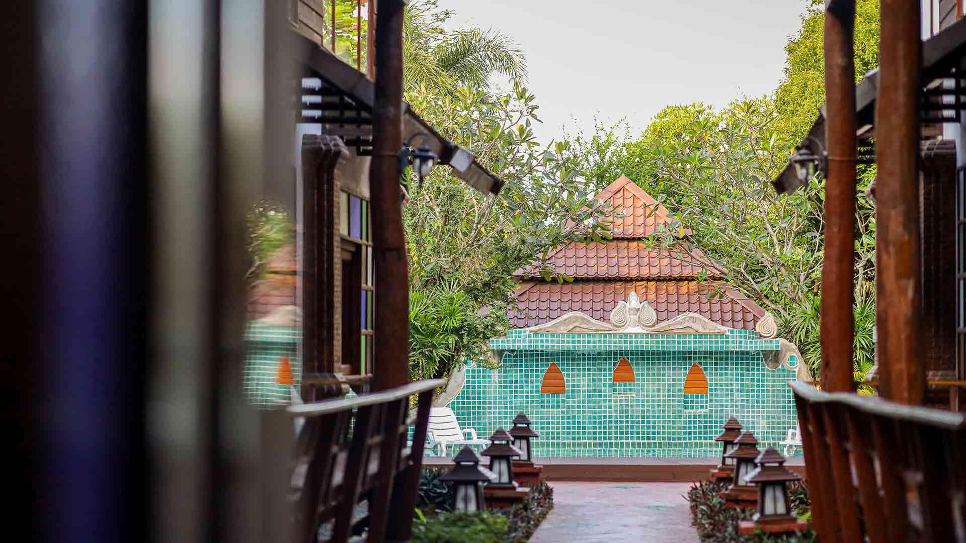 Pathway between Lanna buildings with stone lanterns and teal-tiled sala at Jintara Rehab
