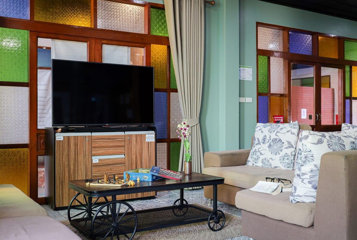 Community lounge with chess set, TV, and coloured stained glass panels at Jintara rehab Chiang Mai