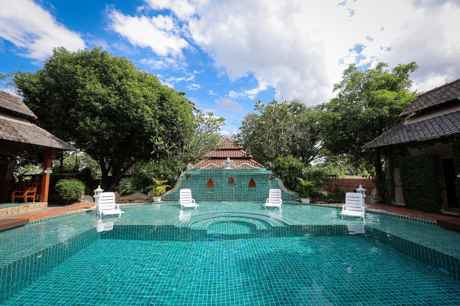 Turquoise pool flanked by teak pavilions and tropical trees at Jintara Rehab in Chiang Mai