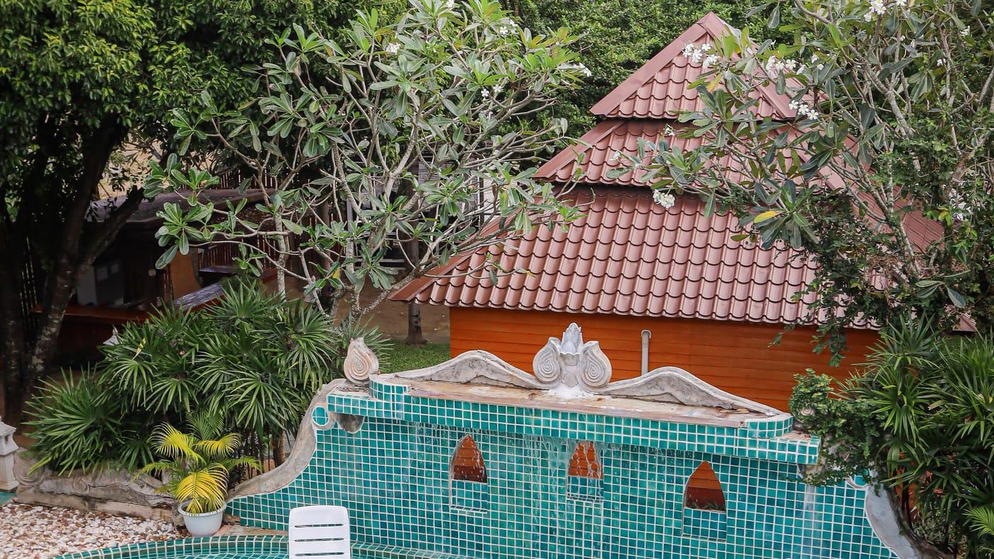 Tiled fountain wall below a pavilion roof and frangipani trees at Jintara Rehab in Chiang Mai