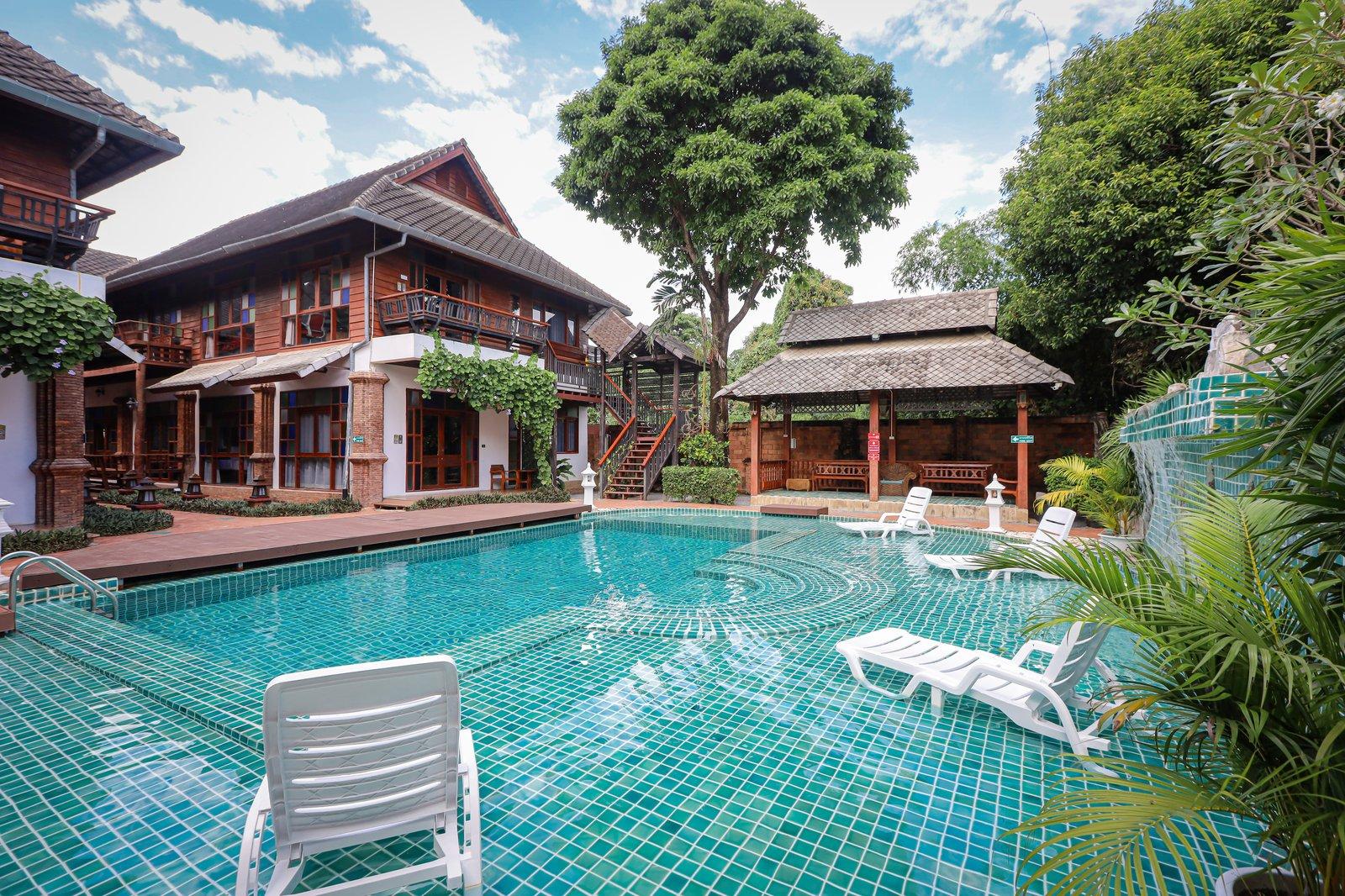 Daytime pool courtyard with teak residential buildings and open sky at Jintara Rehab in Chiang Mai