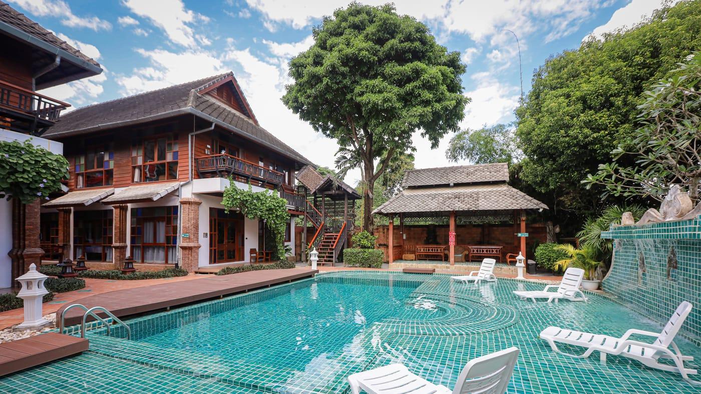The pool, teak buildings and garden pavilion at Jintara Rehab in Chiang Mai under a blue sky