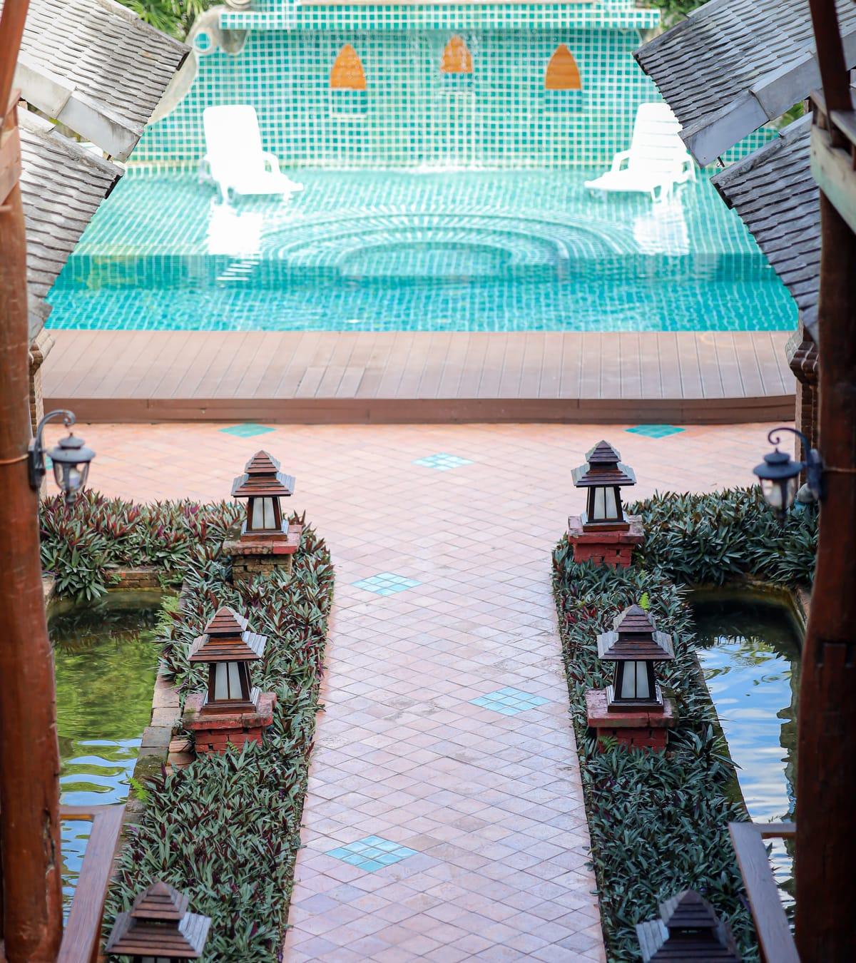A tiled garden path lined with wooden lanterns and plants, leading to the pool at Jintara Rehab in Chiang Mai