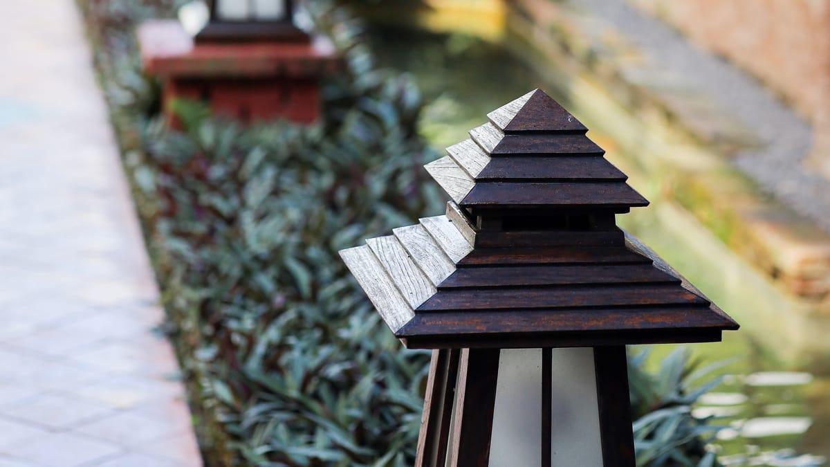 A carved wooden lantern in a planted bed beside a garden path at Jintara Rehab in Chiang Mai