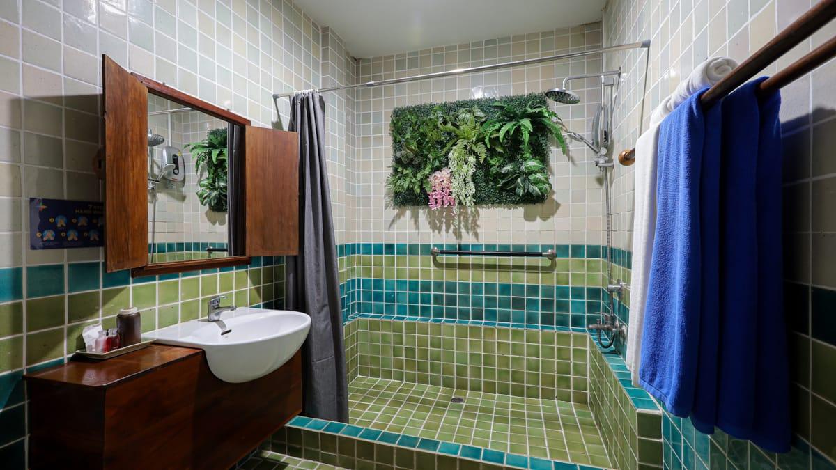 A tiled shower room with a basin, grab rail and plant wall at Jintara Rehab in Chiang Mai