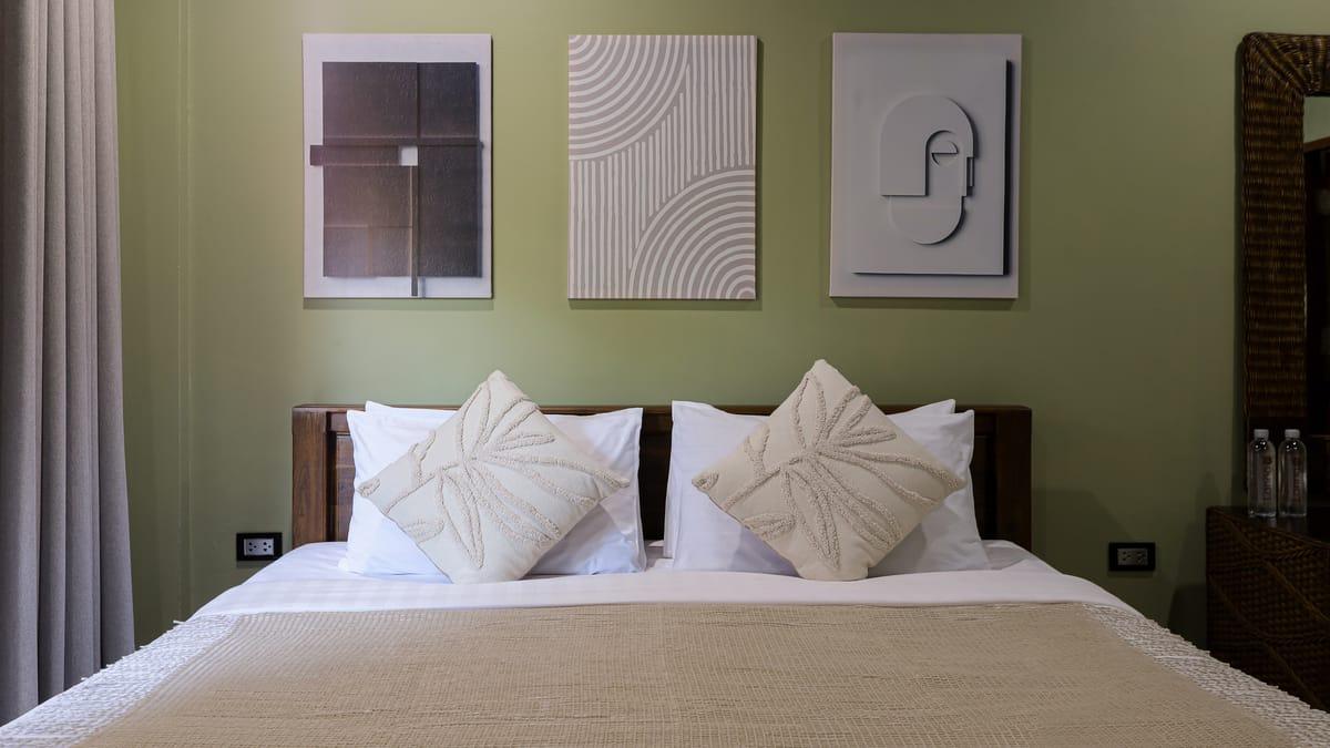 A made bed with white cushions under three wall panels in a bedroom at Jintara Rehab in Chiang Mai