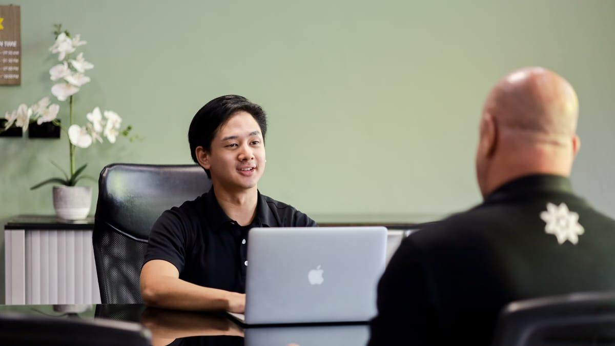 Two men talk across a desk in an office at Jintara Rehab in Chiang Mai