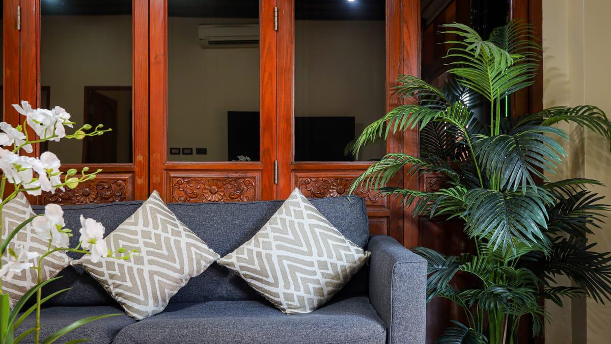 A grey sofa with patterned cushions in front of carved teak doors at Jintara Rehab in Chiang Mai