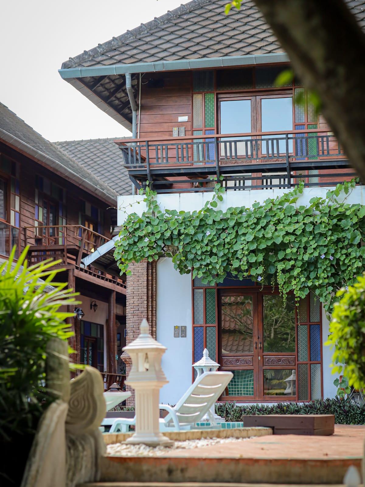 A teak building with a vine-covered balcony in the garden at Jintara Rehab in Chiang Mai